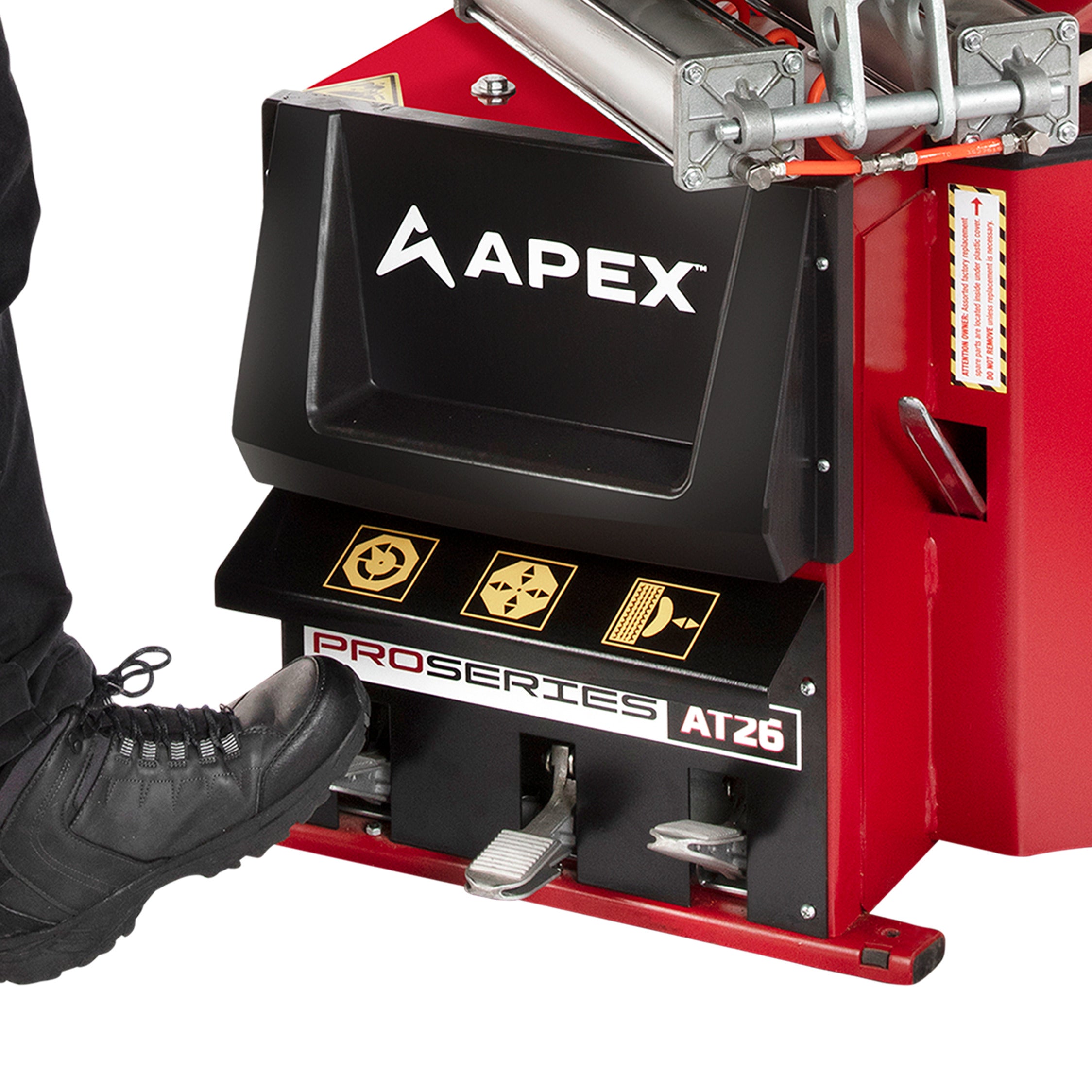 Technician operating the foot pedals on an APEX AT26 tire changer to control reversible turntable rotation.