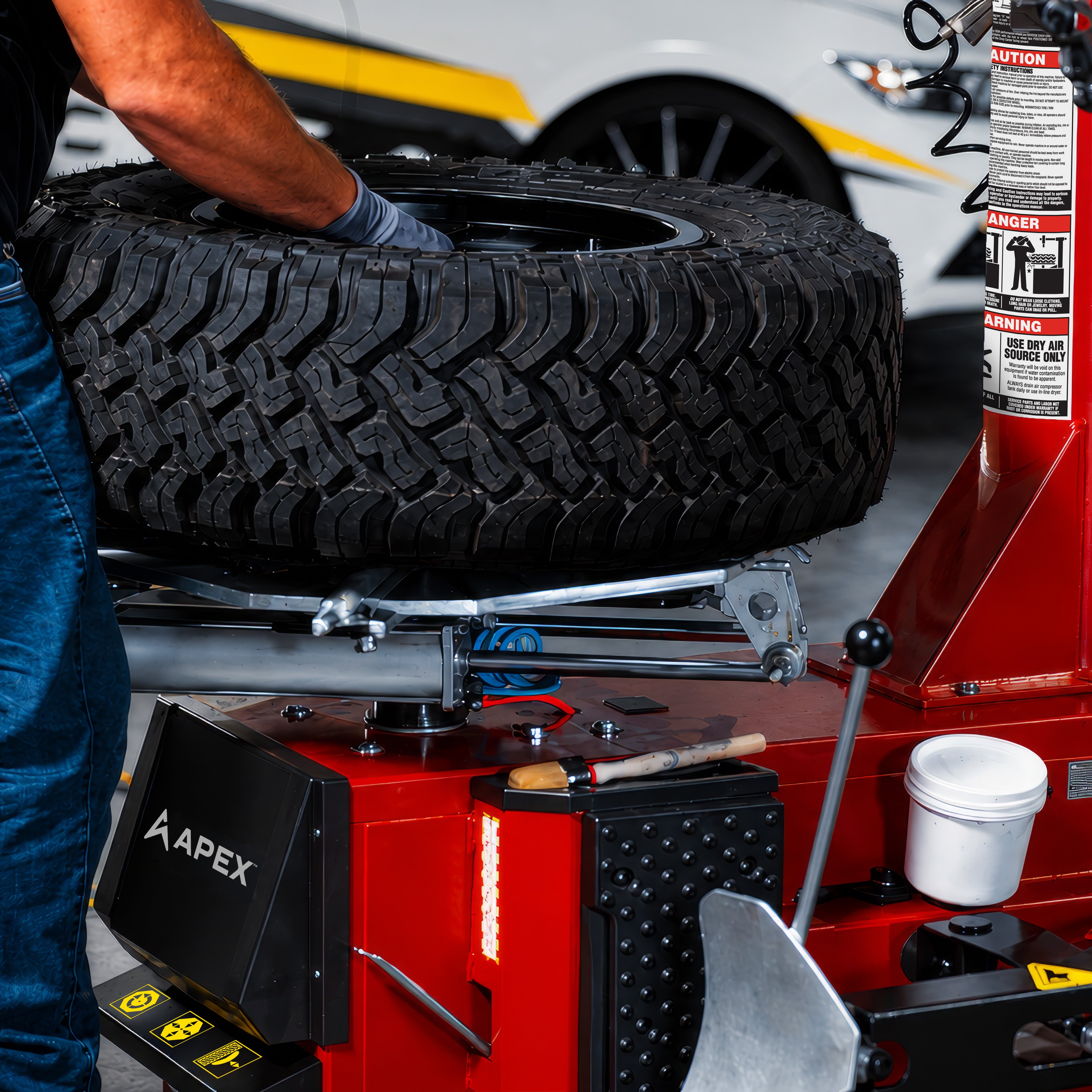 Mechanic using an APEX AT26 automatic tire changer to mount a tire onto a wheel in a commercial automotive shop.