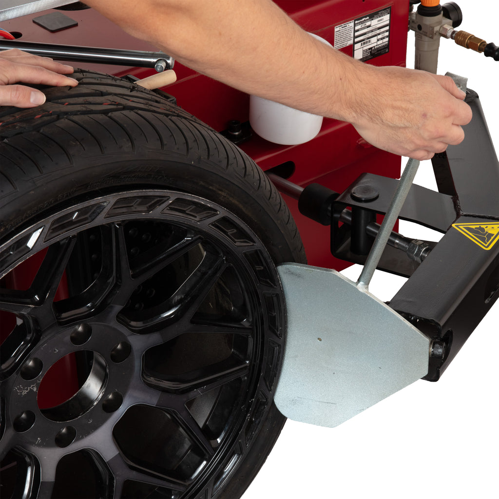 Pneumatic bead-breaker blade separating a tire bead from the wheel rim on an APEX AT26 tire changer.