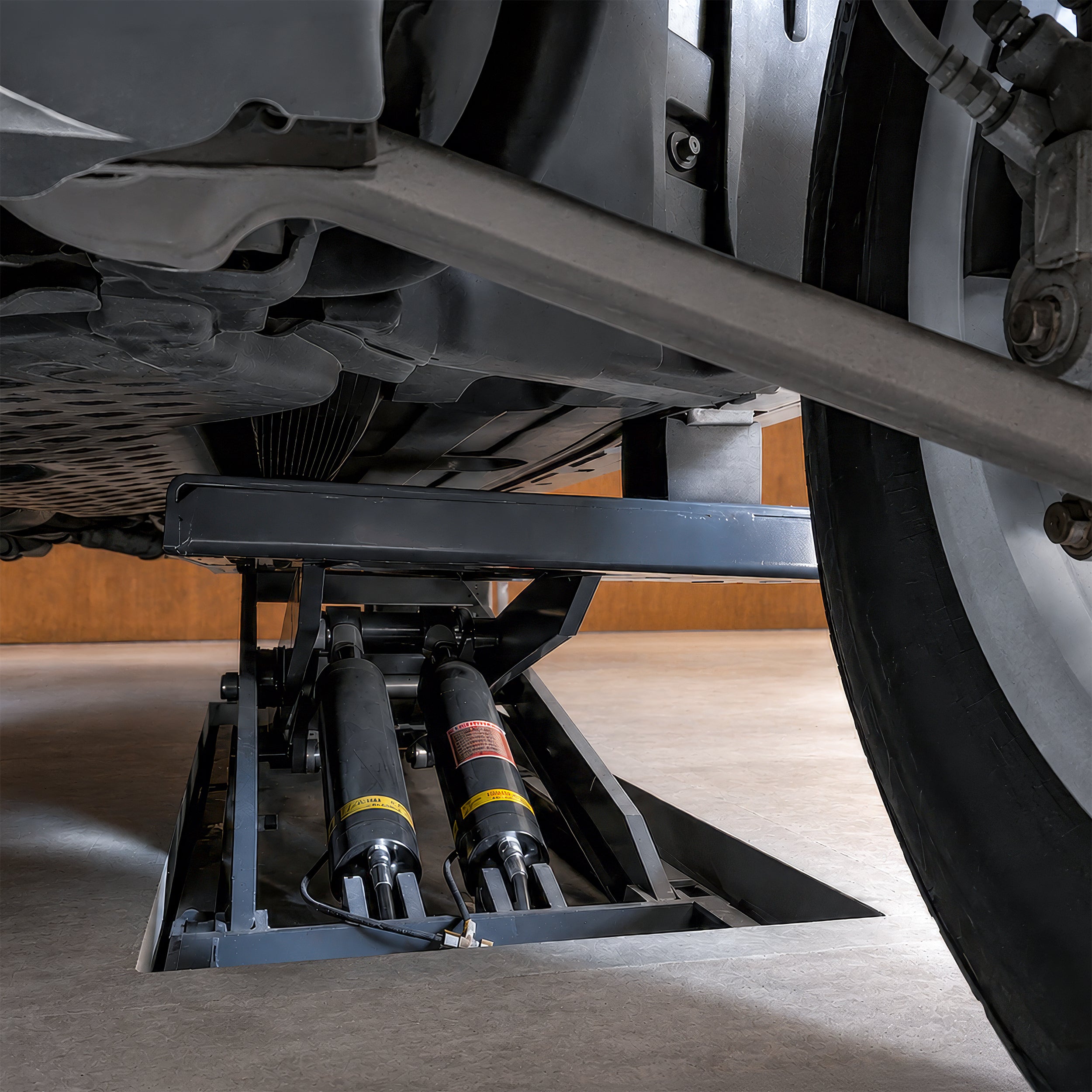 Hydraulic cylinders beneath the platforms of a BendPak MDS-6EXF flush-mount frame-engaging scissor lift.
