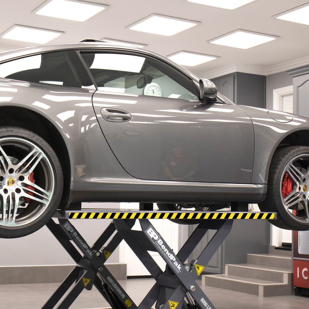 Vehicle raised on the extended platforms of a BendPak MDS-6LP mid-rise scissor lift to reach additional OEM lifting points.