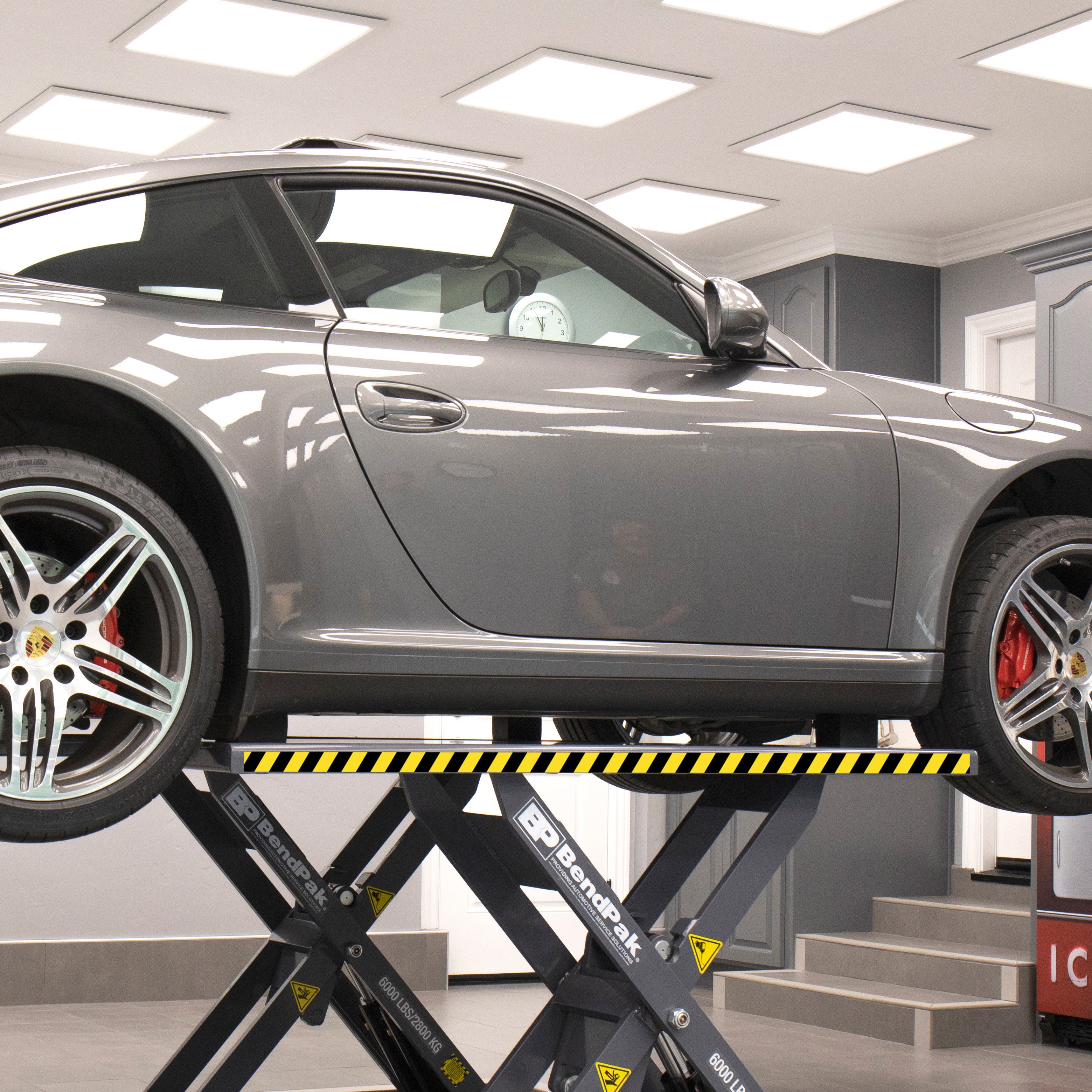 Vehicle raised on the extended platforms of a BendPak MDS-6LP mid-rise scissor lift to reach additional OEM lifting points.