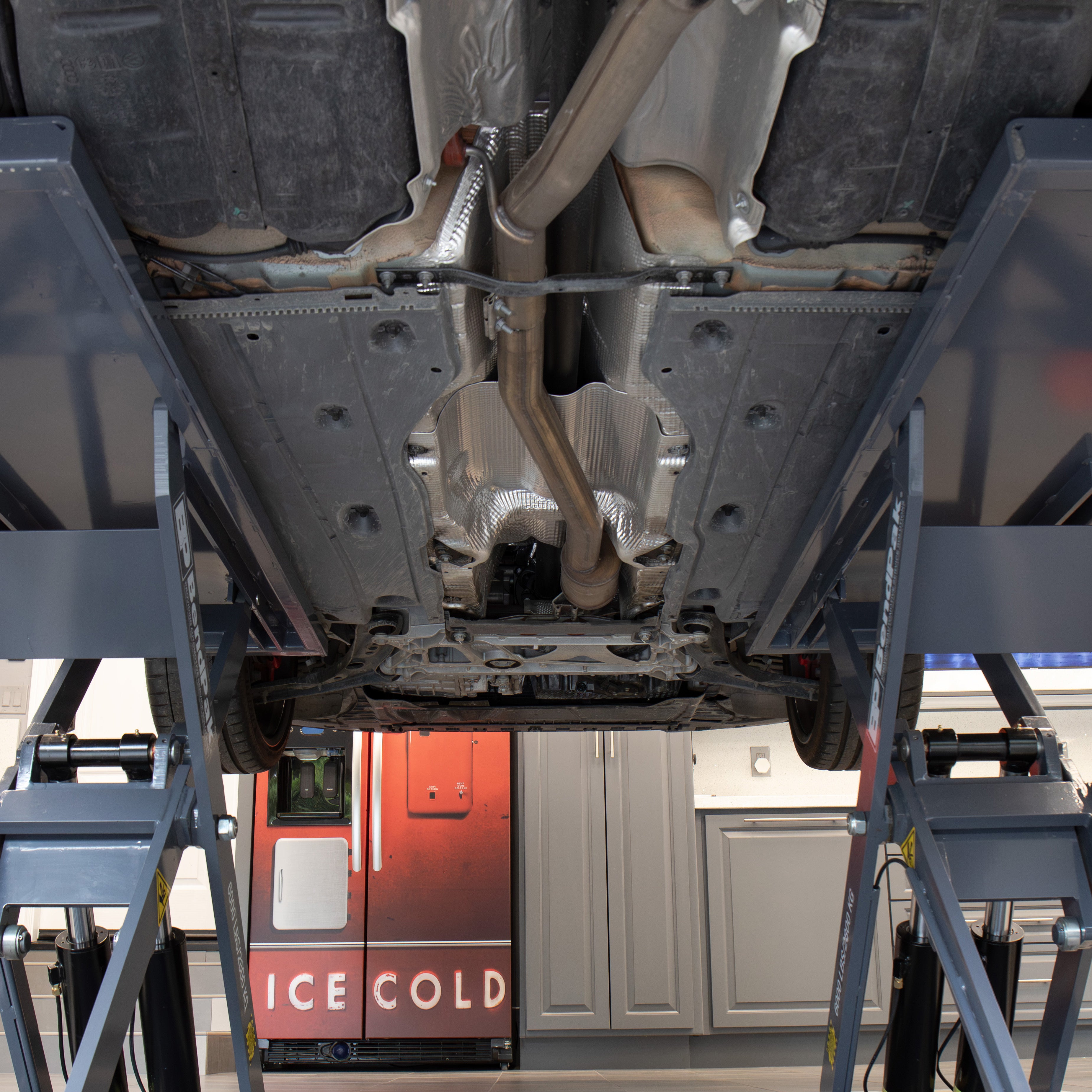 Vehicle undercarriage accessible through the open-center design of a BendPak MDS-6LP mid-rise scissor lift in a garage.
