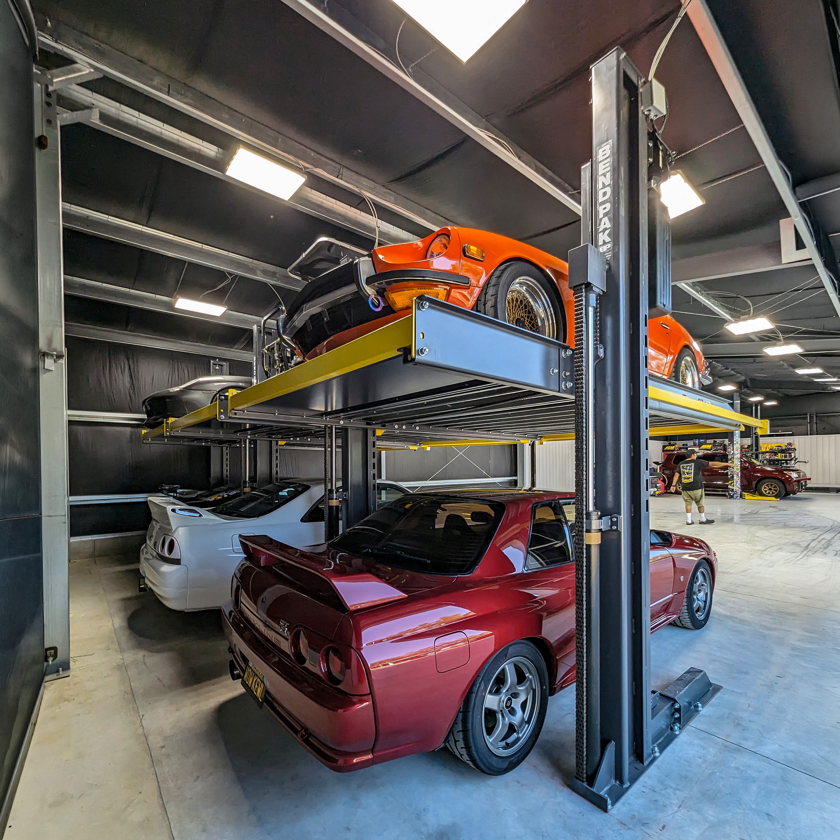 Two cars stacked on a BendPak PL-6000DC two-post parking lift inside a modern garage.