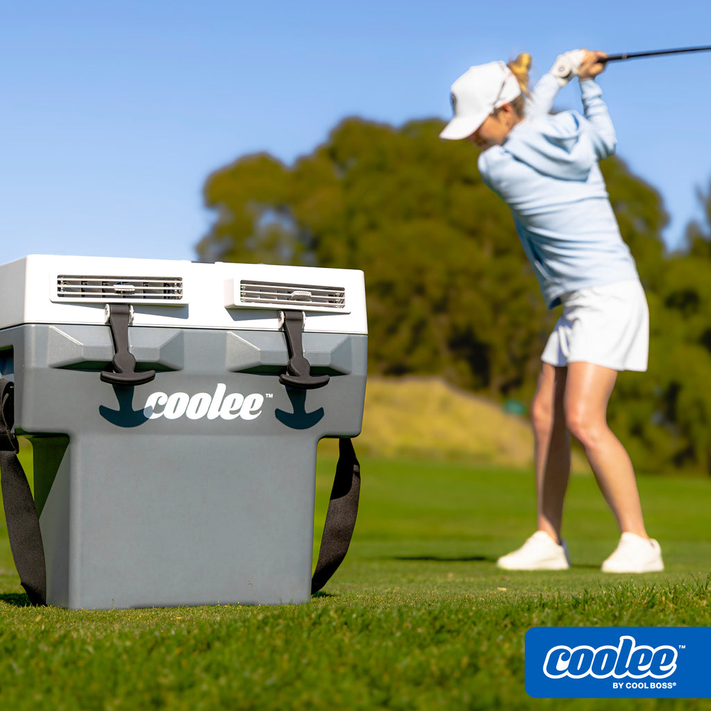 Female golfer swinging a club near a golf cart fitted with a Cool Boss COOLEE TOUR LX portable air cooler.
