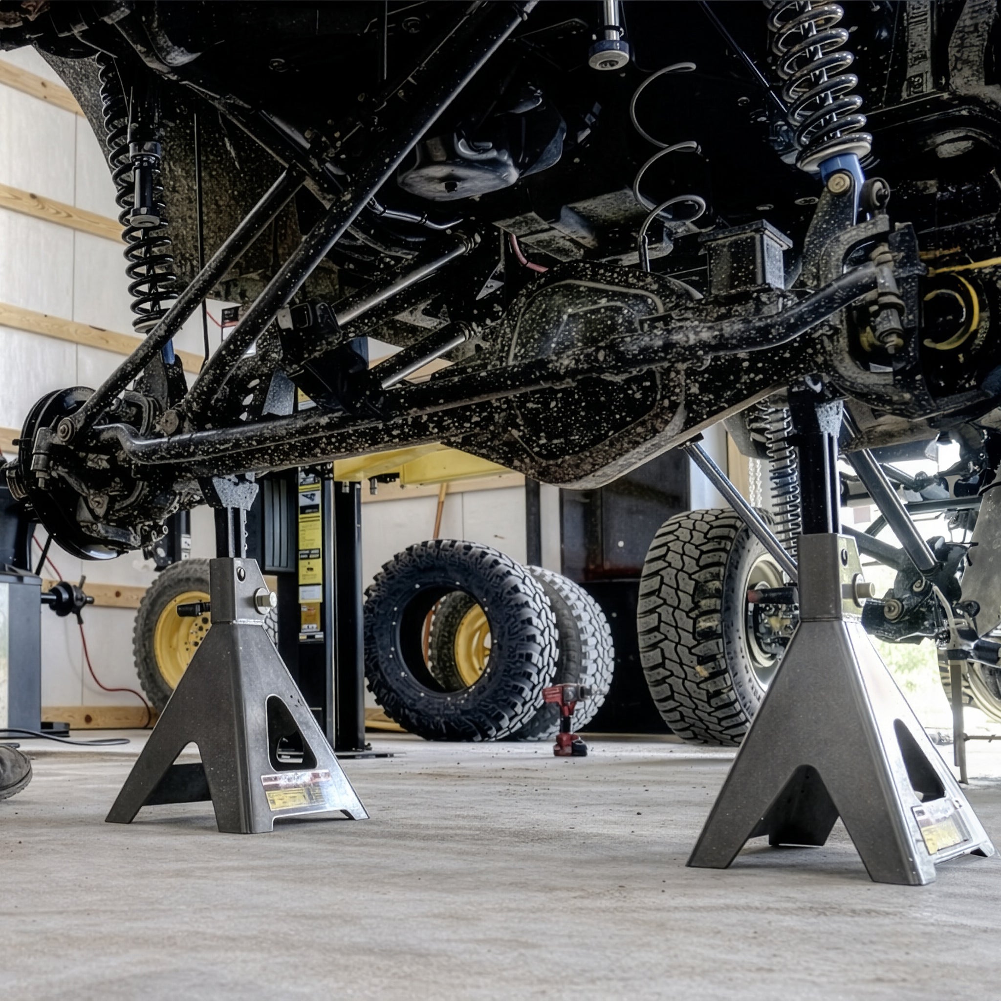 Pair of Ranger RJS-6T 6-ton jack stands supporting the axle of a heavy-duty off-road vehicle in an industrial shop.